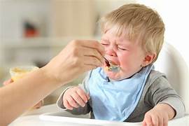 Worried mother trying to feed baby who is refusing food, highlighting potential feeding difficulties in infants